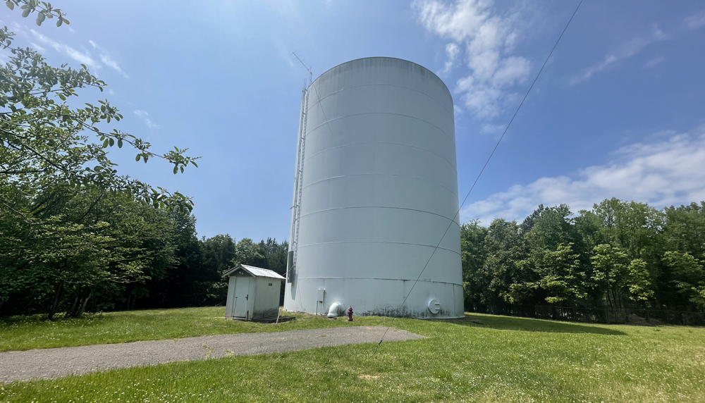 A large ground storage water tank with an adjacent equipment shed, set on a grassy site surrounded by trees, part of Water Authority of Dickson County's water system infrastructure.